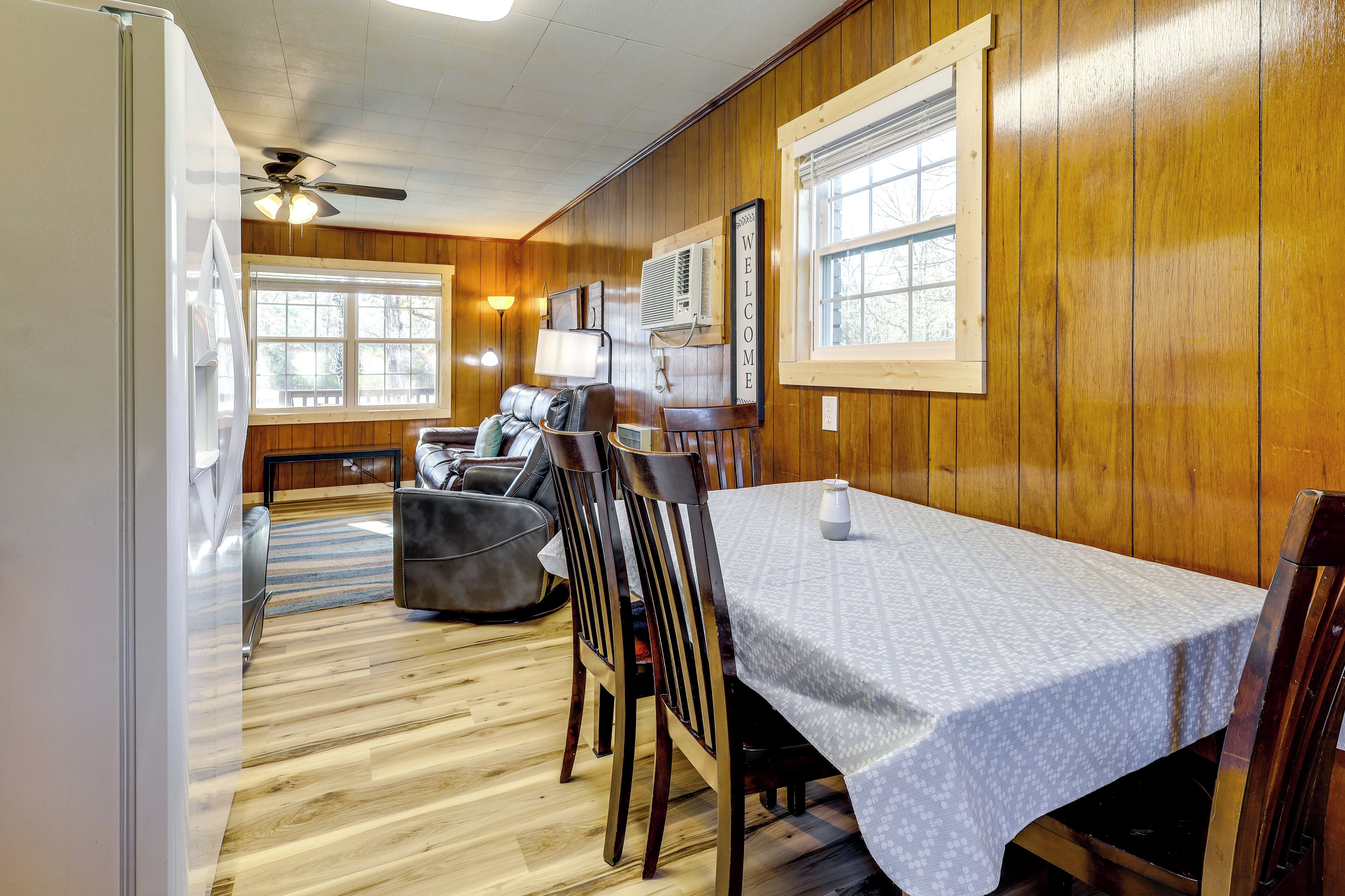 A dining area with a table set for two, wooden walls, a ceiling fan, and a window with a view.