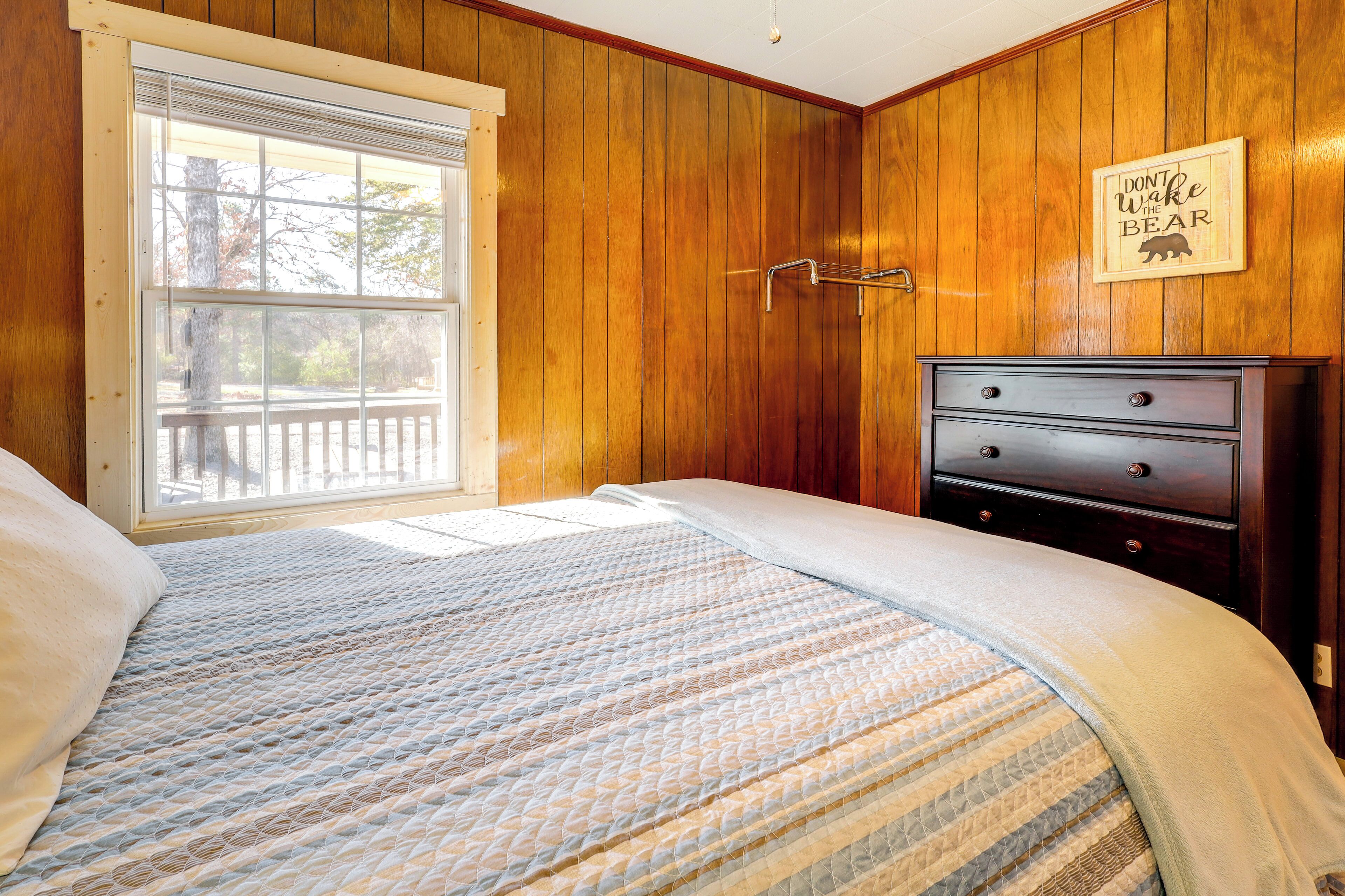 Ein Schlafzimmer mit Holzwandverkleidung, einem Fenster mit Blick und einem Bett mit gemustertem Überwurf, sowie eine Kommode mit Schubladen.