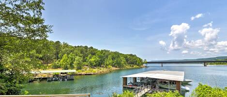 A lakeside property with docked boats, a covered boat house, and a bridge in the background.