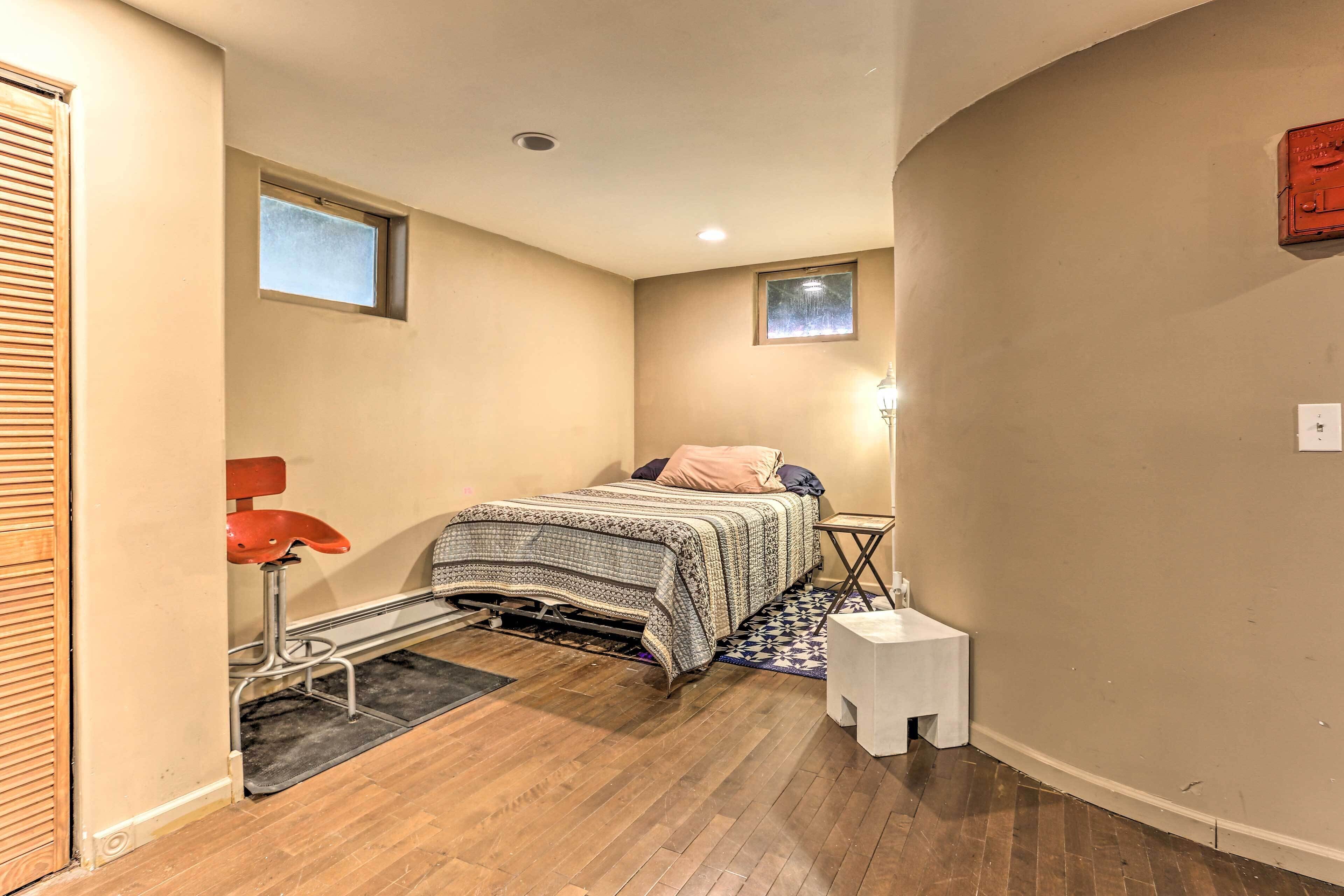 A bedroom with a bed, a small bedside table, a nightstand, a window, and a door.