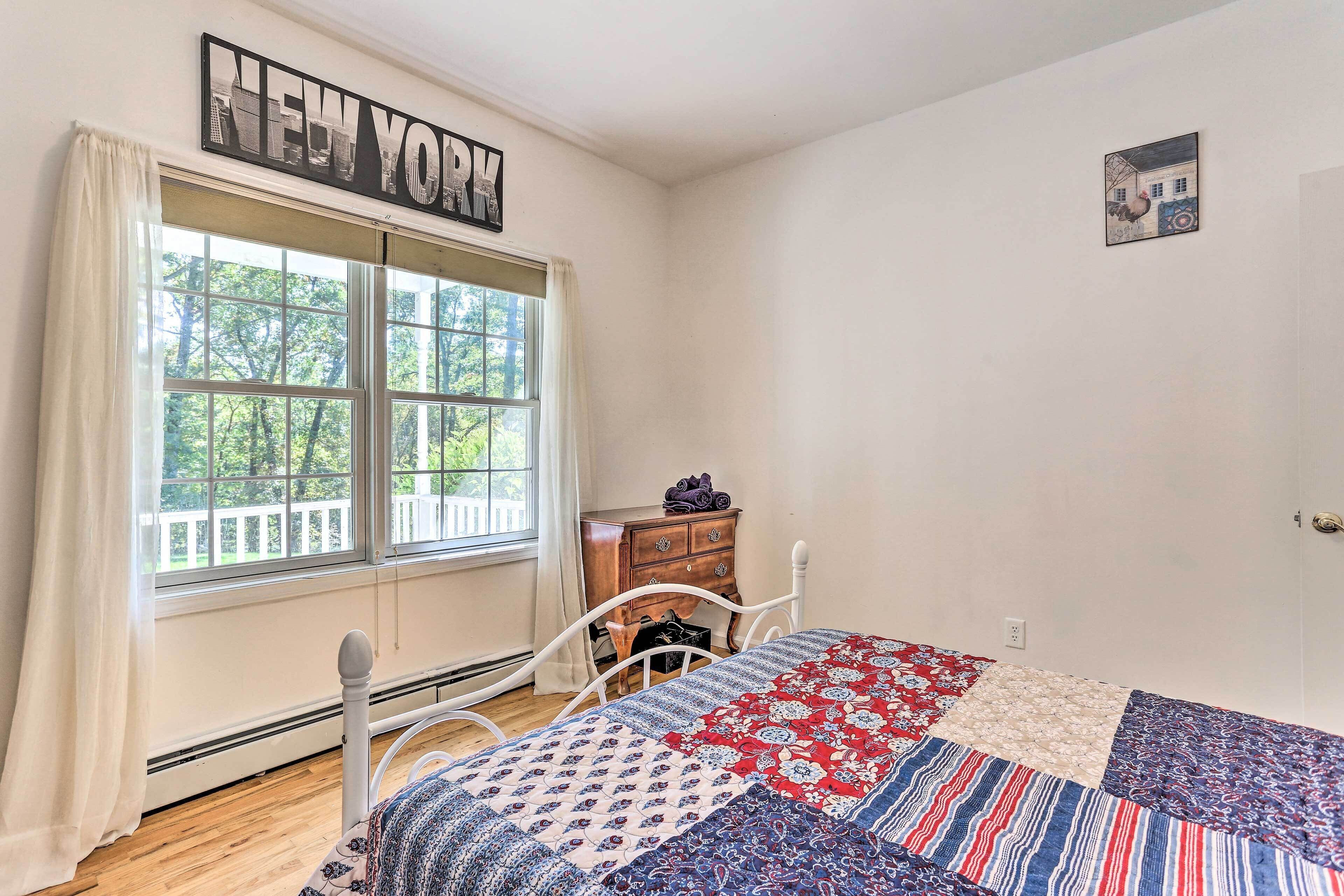 Une chambre à coucher avec un lit, une commode, une fenêtre avec des rideaux et un panneau mural sur lequel on peut lire « NEW YORK ».