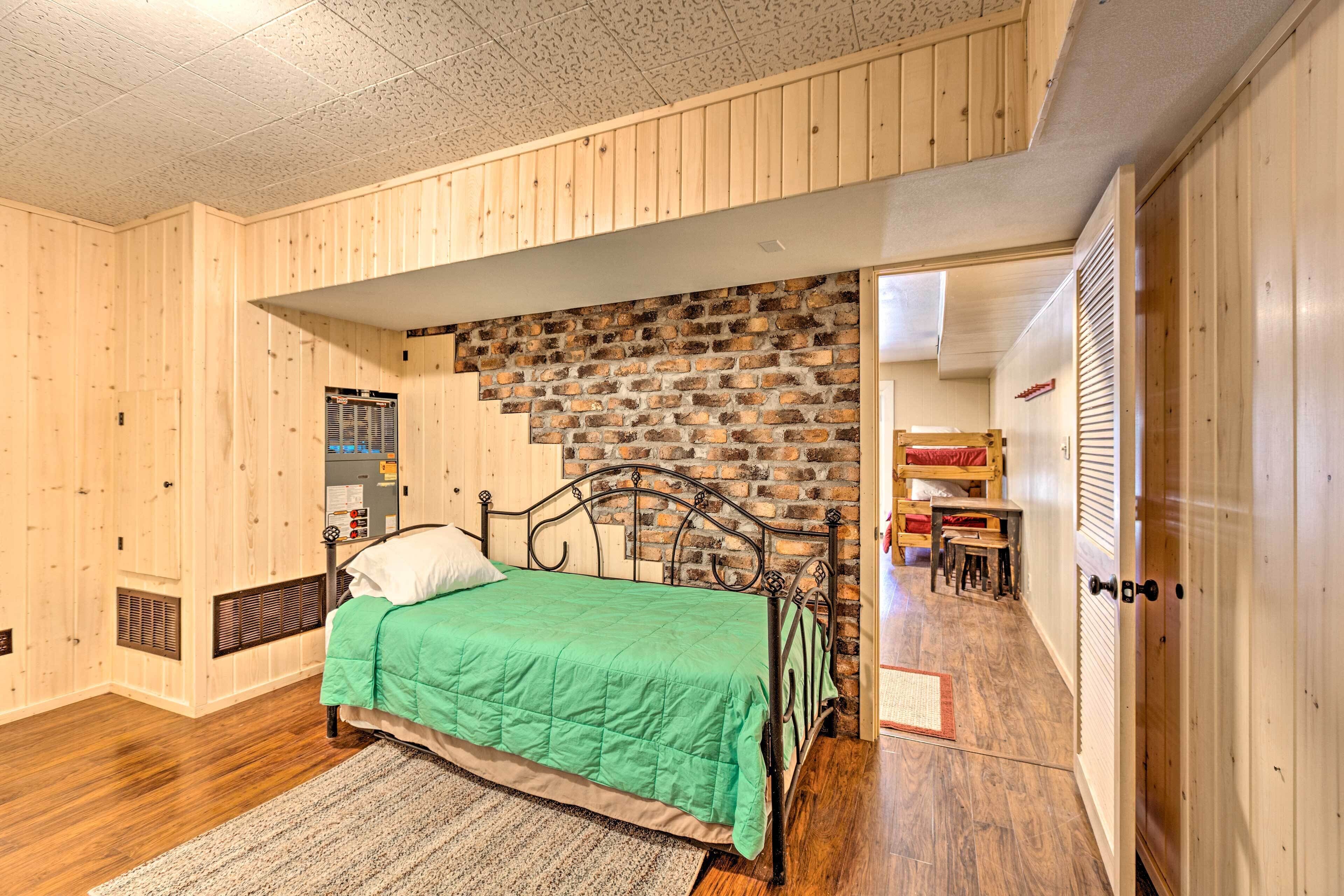 A bedroom with a green bed, wooden walls, a brick accent wall, and a wooden ceiling.