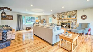 A spacious living room with a large sofa, a wooden coffee table, and a stone fireplace. - Family Winter Retreat w/ Hot Tub: 14 Mi to Slopes! (Whitingham)