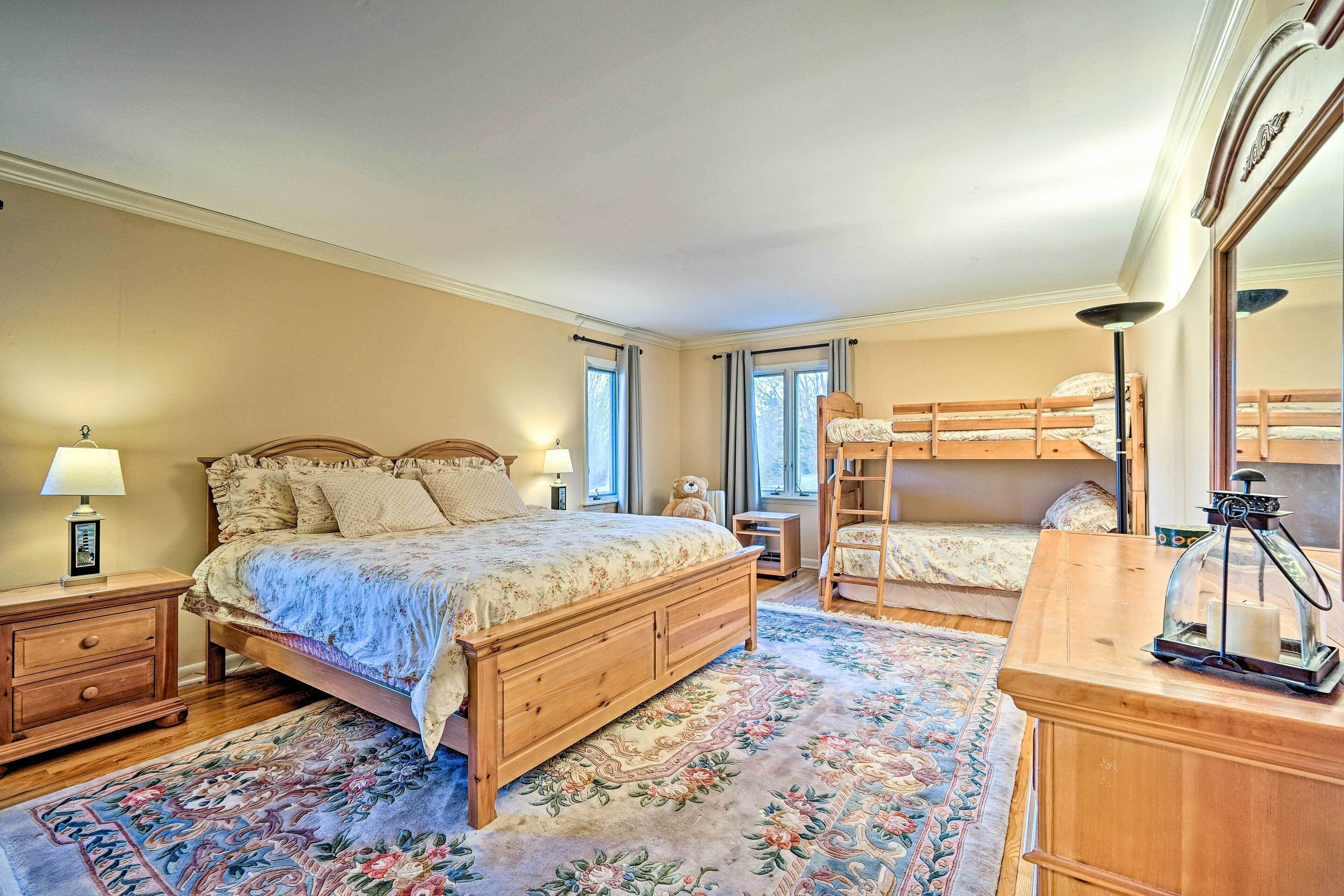 A bedroom with a large bed, a wooden dresser, a nightstand, a lamp, a mirror, and a bunk bed.