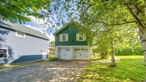Une maison à deux étages avec un garage, entourée d’une pelouse bien entretenue et d’arbres.