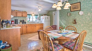 Une cuisine avec des meubles de rangement en bois, une table à manger avec des chaises et un ventilateur de plafond.