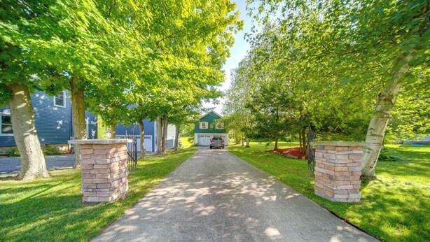 Une allée menant à une maison avec un garage, entourée d’arbres et bordée d’une pelouse bien entretenue.