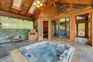 A wooden cabin with a hot tub, stone wall, and large windows.