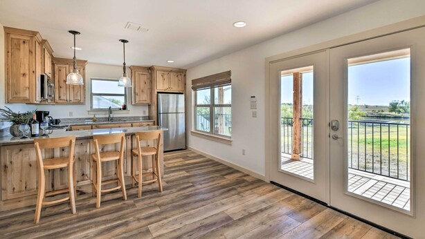 A spacious kitchen with wooden cabinets, a central island with bar stools, and a large window overlooking a scenic outdoor area. - Dog-friendly Apartment ~ 32 Mi to Fort Worth! (Godley)