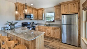 A kitchen with wooden cabinets, a stainless steel refrigerator, granite countertops, and pendant lighting. - Dog-friendly Apartment ~ 32 Mi to Fort Worth! (Godley)