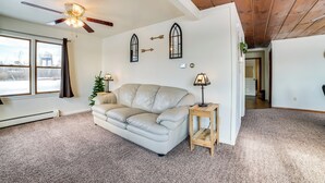 A living room with a beige leather sofa, a small wooden side table, a ceiling fan, and two wall-mounted lamps.