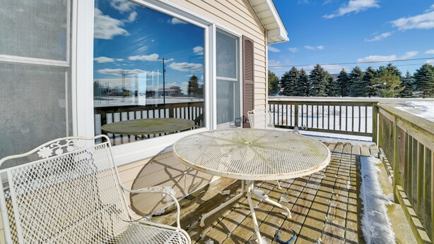 A covered outdoor patio with a round table and two chairs, large sliding glass doors, and a view of trees and a building in the background.