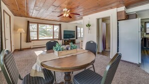 A dining area with a wooden ceiling, a ceiling fan, a television, and a dining table with chairs.