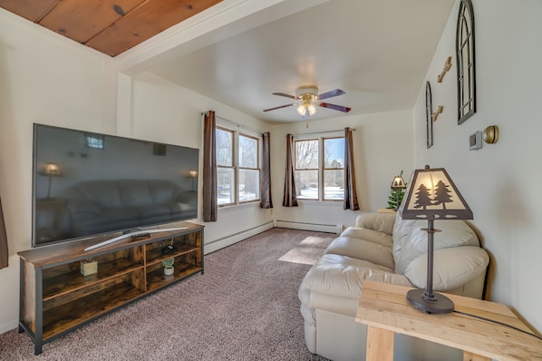 A living room with a flat-screen TV, wooden entertainment unit, beige sofa, and a ceiling fan. - Cozy Tawas City Home w/ Views of Lake Huron! (Tawas City)