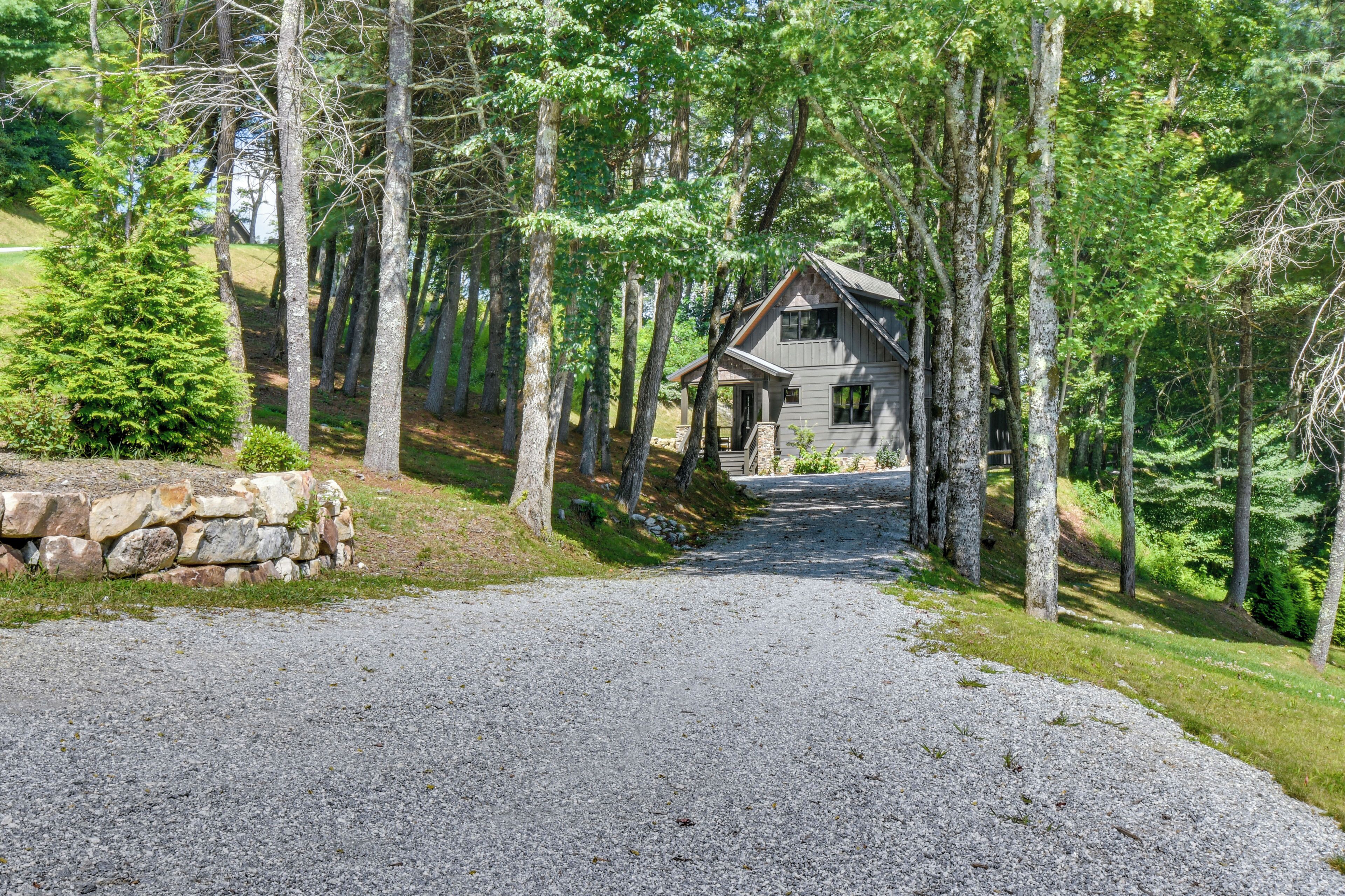 A cabin surrounded by tall trees, with a gravel driveway leading to it.