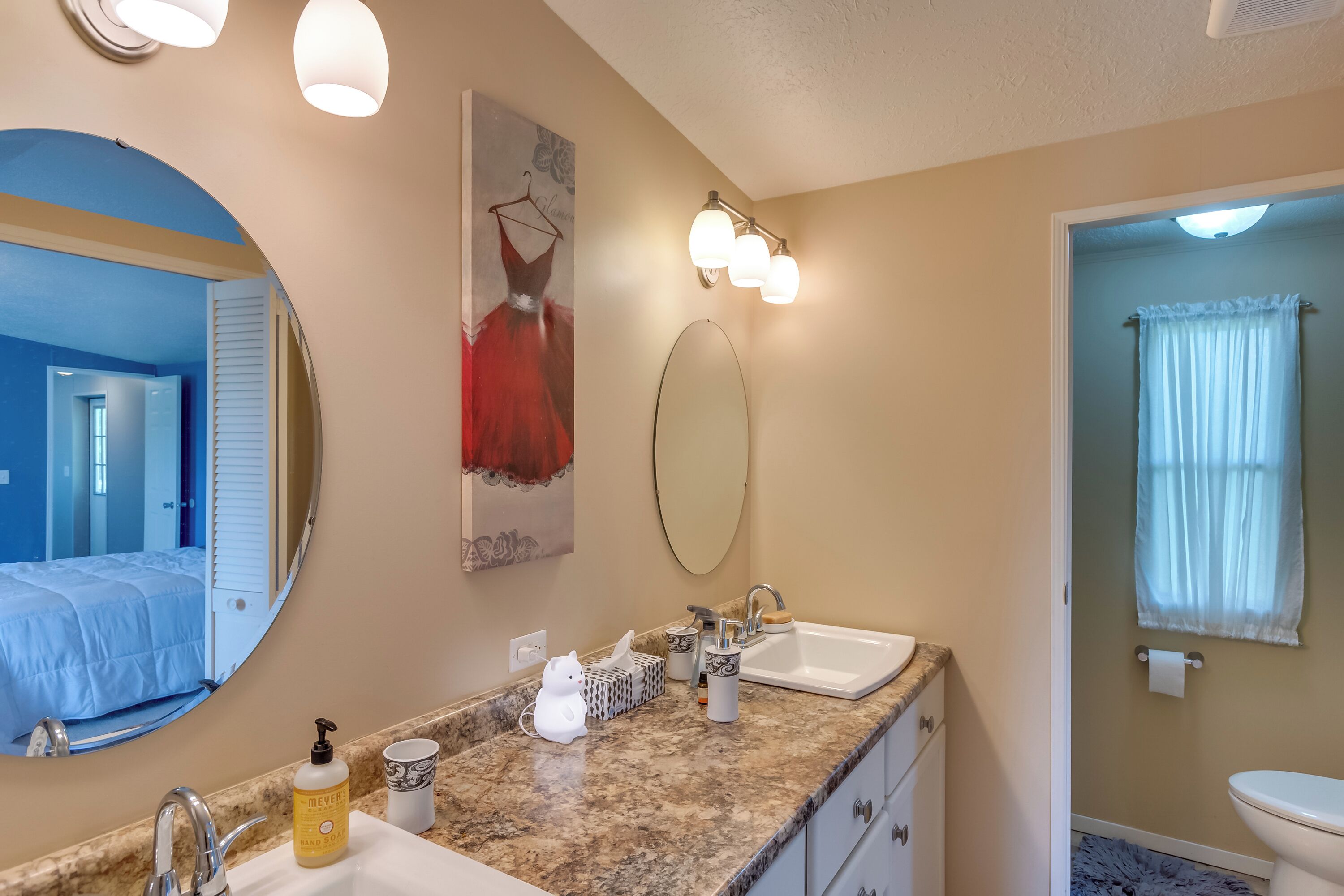 Une salle de bain avec un lavabo, un miroir et un porte-serviettes. Une serviette est accrochée au mur et un flacon de savon liquide est posé sur le comptoir.