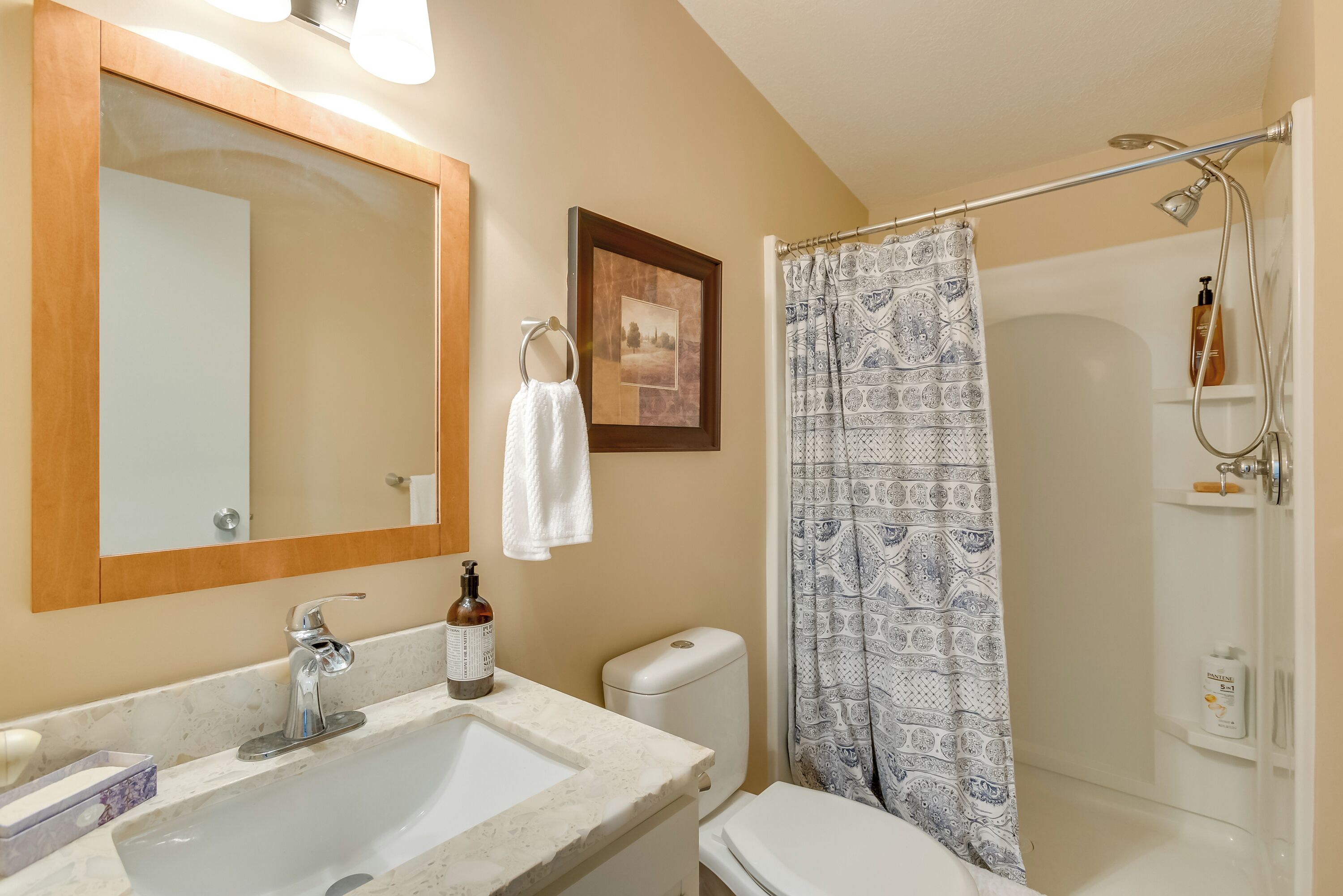 A bathroom with a sink, mirror, toilet, shower, and towel rack.