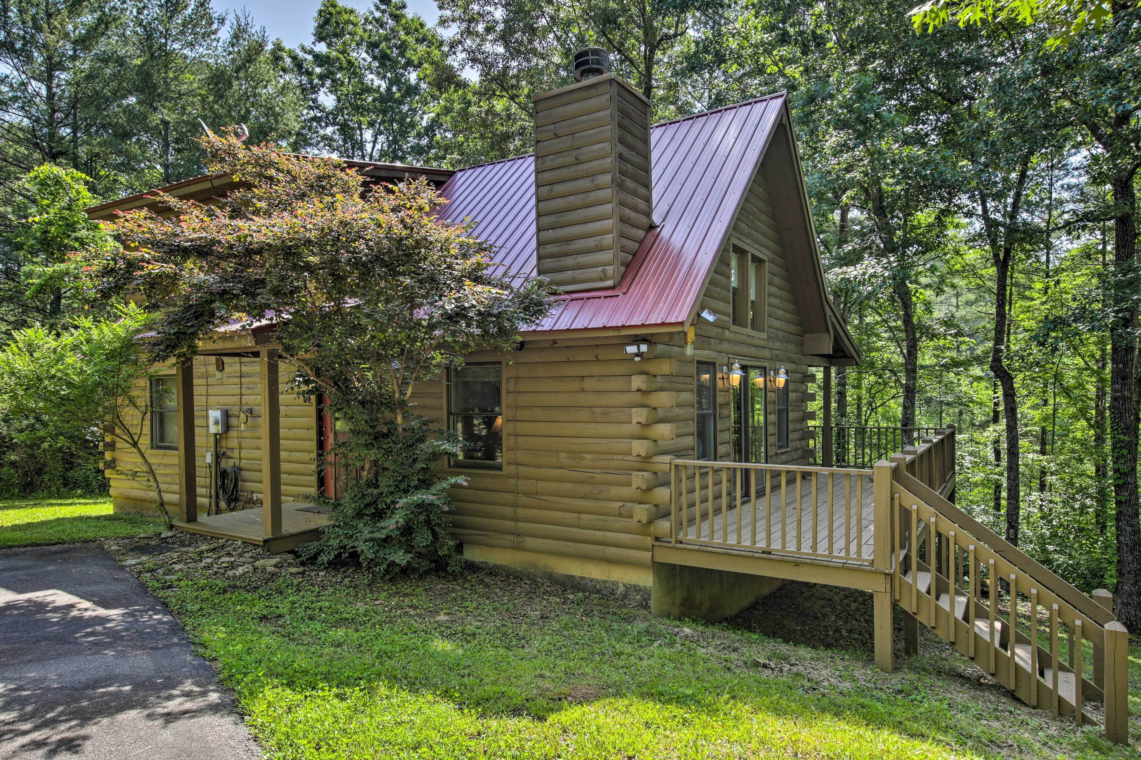 A log cabin with a metal roof, a wooden deck, and a staircase leading to the entrance.