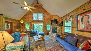 L’intérieur d’un chalet confortable, avec un grand canapé, une cheminée et un ventilateur de plafond.