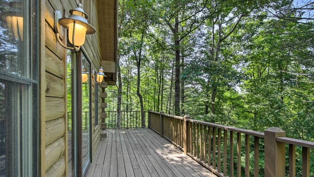 Une terrasse en bois, dotée de portes et de fenêtres en verre, entourée d’une balustrade en bois, et offrant une vue sur une zone boisée.