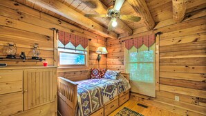 Une chambre à coucher dans une cabane en bois, avec un lit, une table de chevet, une lampe et une fenêtre avec des rideaux.
