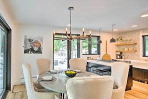 Uma área de refeições moderna com uma mesa redonda, seis cadeiras e um candelabro.