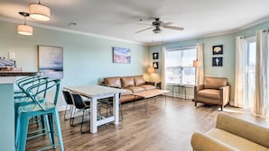 A living room with a sofa, chairs, a coffee table, a dining table with chairs, a ceiling fan, and a window with curtains. - Oak Island Condo - Walk to the Beach! (Oak Island)