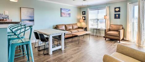 Un salon comprenant un canapé, des fauteuils, une table basse, une table à manger avec des chaises, un ventilateur de plafond et une fenêtre avec des rideaux.