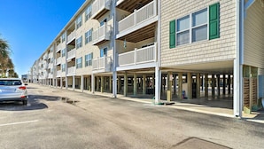 A multi-story building with balconies, a covered parking area, and a clear sky. - Oak Island Condo - Walk to the Beach! (Oak Island)