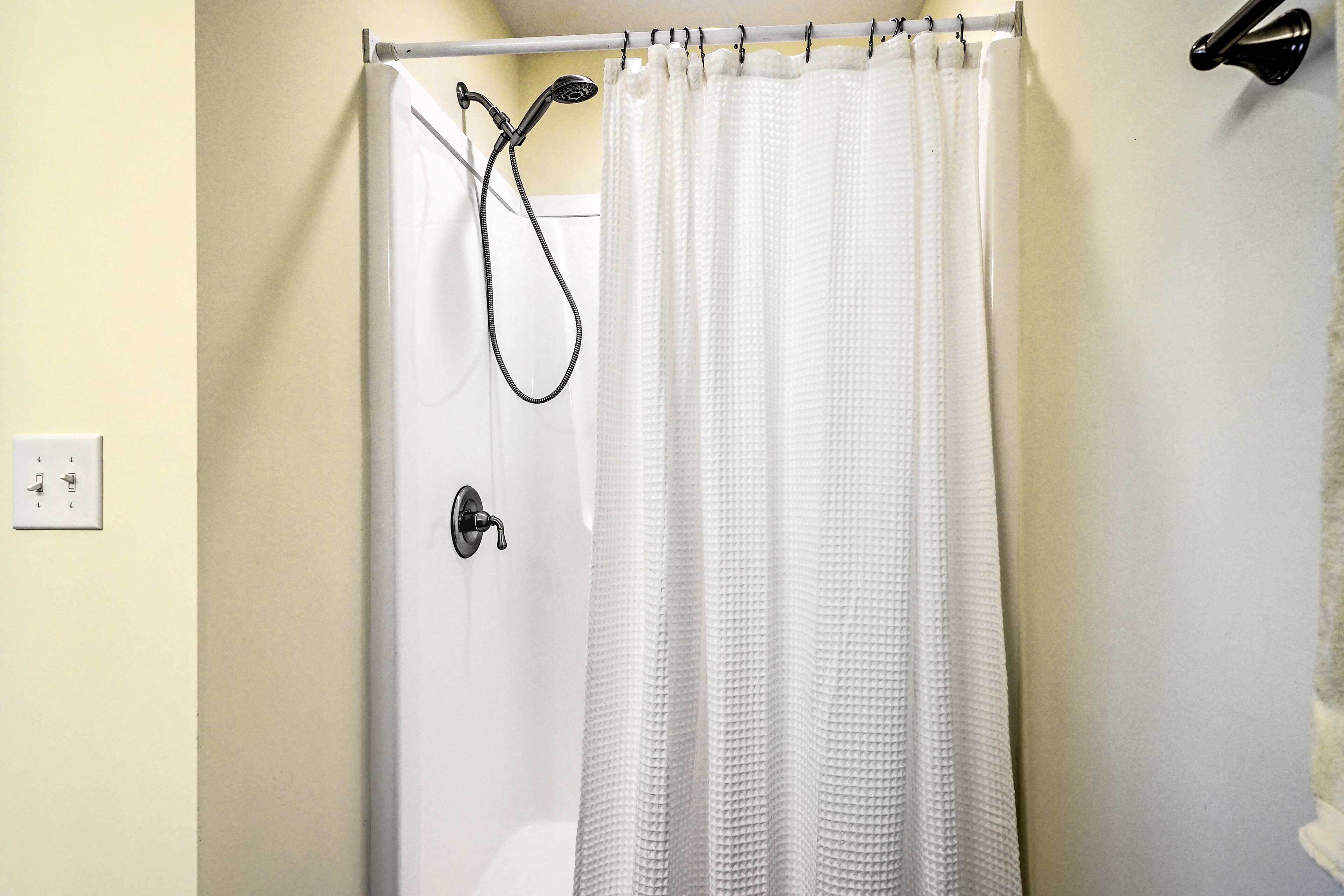 A bathroom with a white shower curtain, a handheld showerhead, and a wall-mounted towel rack.