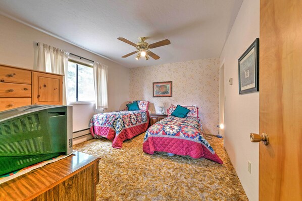 A bedroom with two beds, a ceiling fan, a television, and a window with curtains. - Hideaway on Working Cattle Ranch 26 Mi to Rogerson (Twin Falls)