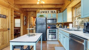 Innenansicht einer Holzhütte mit einer Küche, die einen Kühlschrank, eine Mikrowelle, einen Herd und ein Schild mit der Aufschrift 'SWEET TEA' zeigt.