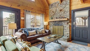 Ein gemütliches Blockhaus-Interieur mit Kamin aus Stein, Holzbalkendecke und einer Couch mit Kissen.