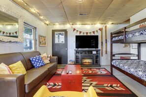 Quarto mobiliado com sofá, mesa de centro vermelha, televisão, lareira e beliche.