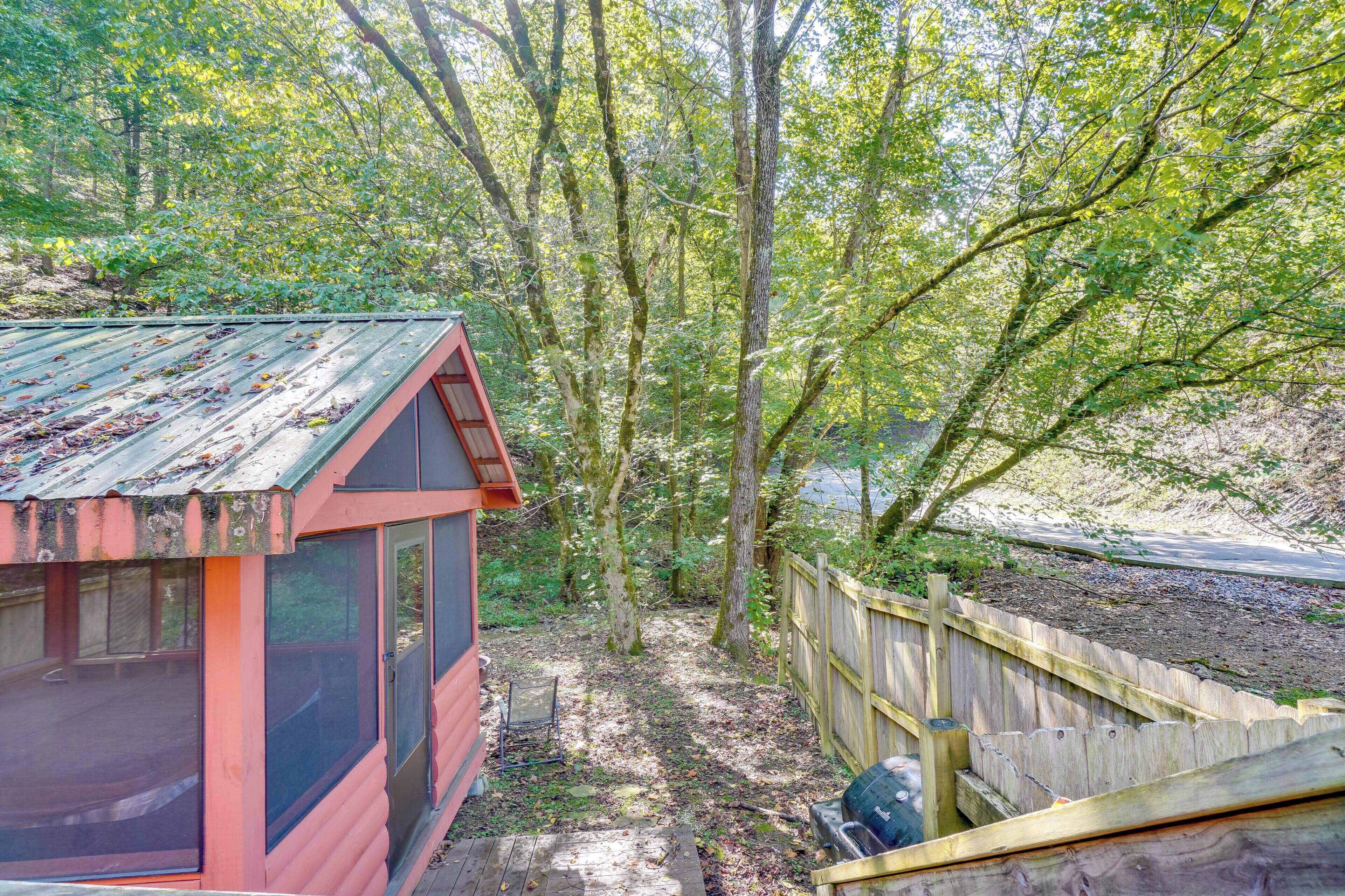 A rustic cabin with a metal roof, surrounded by a wooden fence and dense forest.