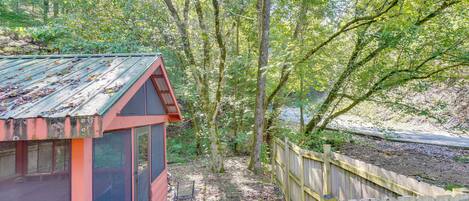 A rustic cabin with a metal roof, surrounded by a wooden fence and dense forest.