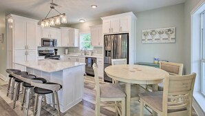 A modern kitchen with white cabinets, stainless steel appliances, a marble island, bar stools, and a dining table with chairs.