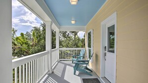 A covered porch with a white railing, a blue Adirondack chair, and a white door.