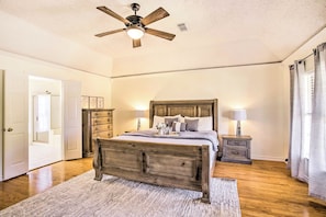 Un dormitorio con cama de madera, mesitas de noche, ventilador de techo y una puerta que da a otra habitación.