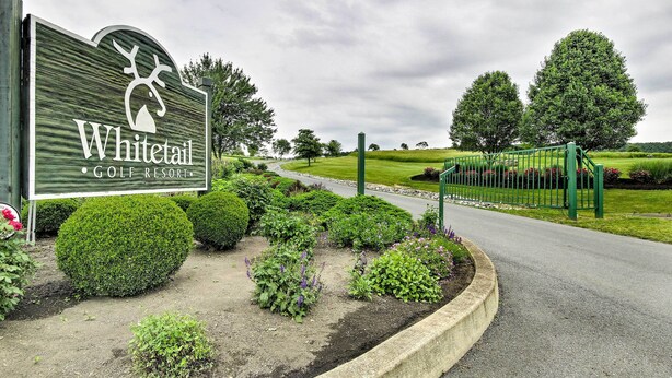 Un panneau indiquant un complexe hôtelier avec un parcours de golf, orné d’un logo représentant un cerf, et entouré de jardins bien entretenus et d’une clôture verte.