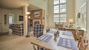 Un salon spacieux doté d’une cheminée, de grandes fenêtres et d’un coin repas avec des chaises et des sets de table à motifs écossais.