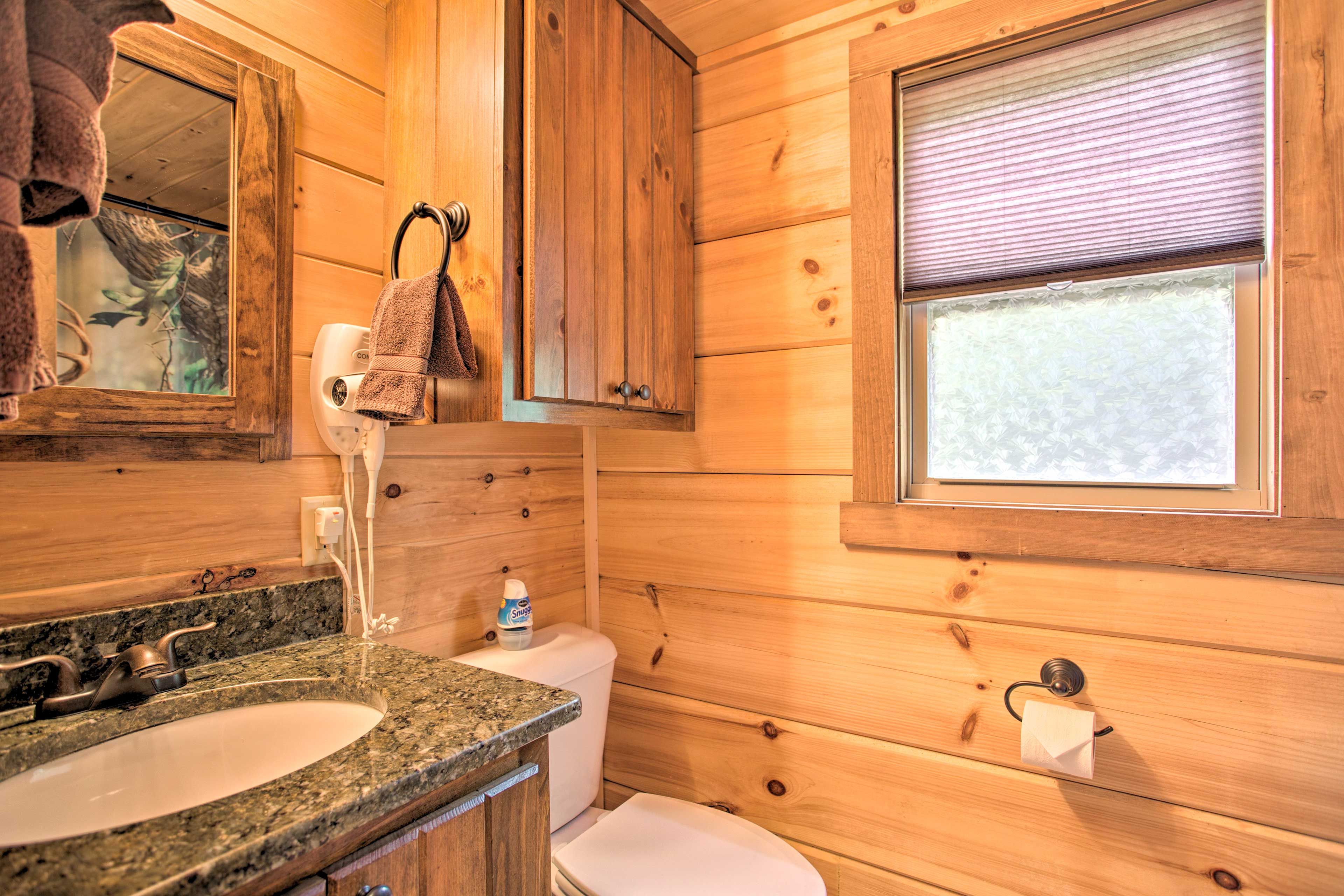 A wooden cabin bathroom with a granite sink, toilet, and a window with blinds.