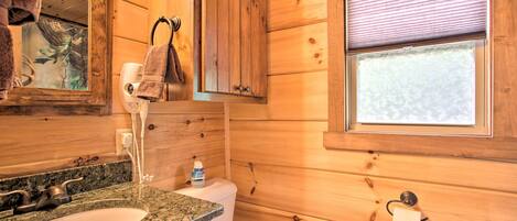 A wooden cabin bathroom with a granite sink, toilet, and a window with blinds.
