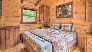 A wooden cabin bedroom with a bed, a window, a ceiling fan, and a framed picture on the wall. - Hike, Sip & Unwind! Mill Spring Cabin Near Winery (Mill Spring)