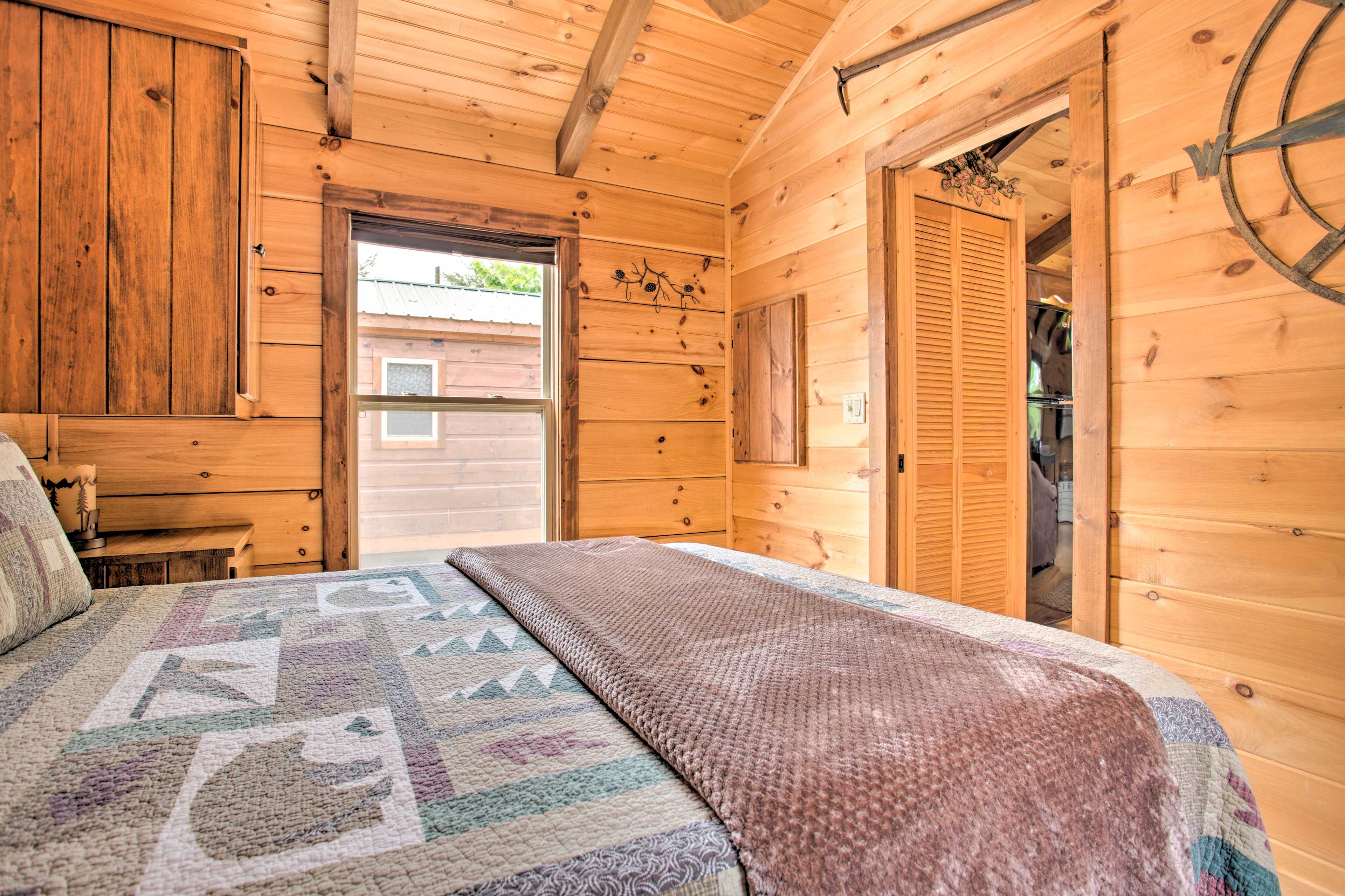 Un dormitorio de cabaña de madera con una cama, un tocador de madera y una puerta que da al exterior.
