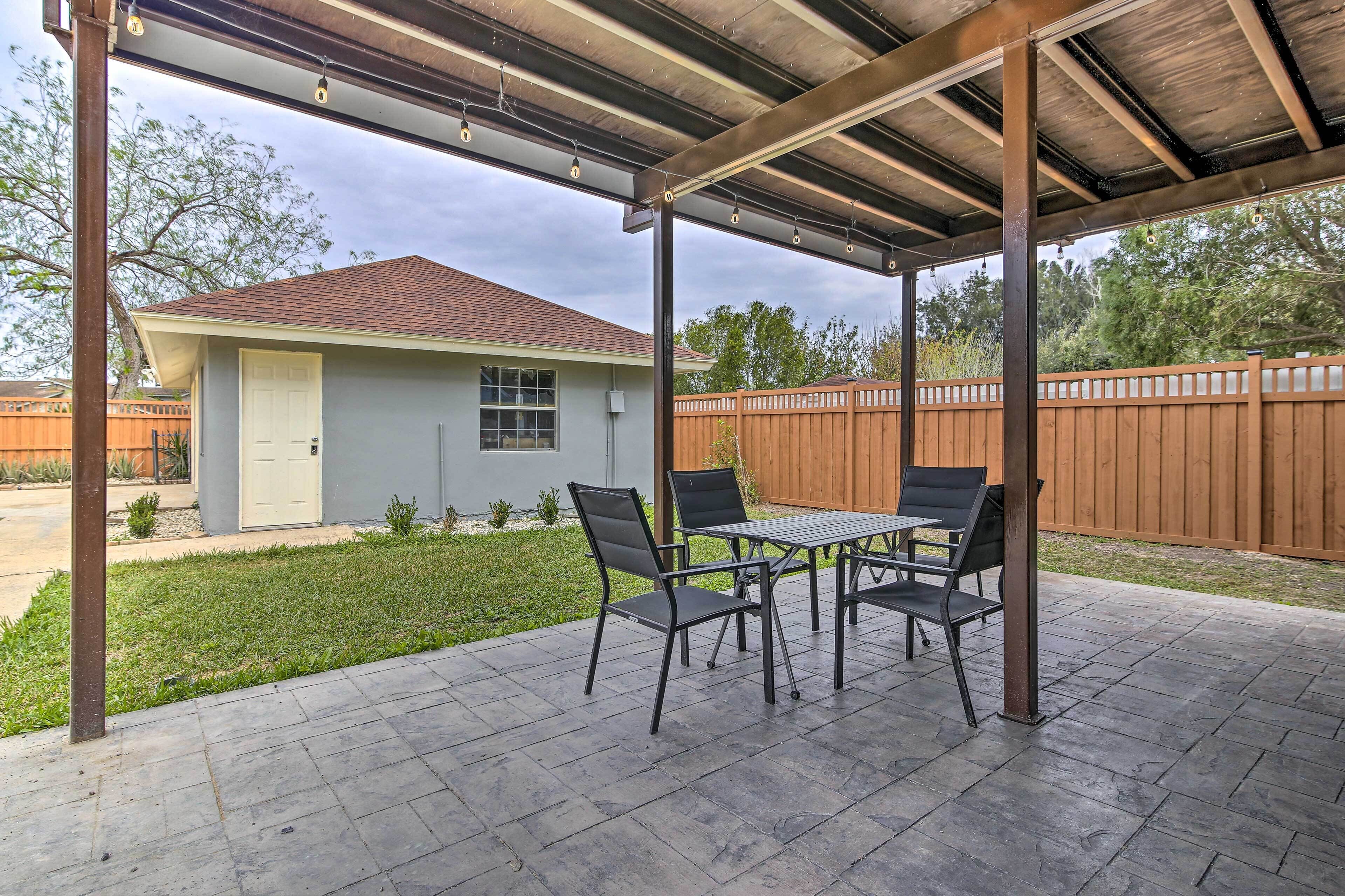 An outdoor patio with a covered seating area, a house in the background, and a wooden fence.