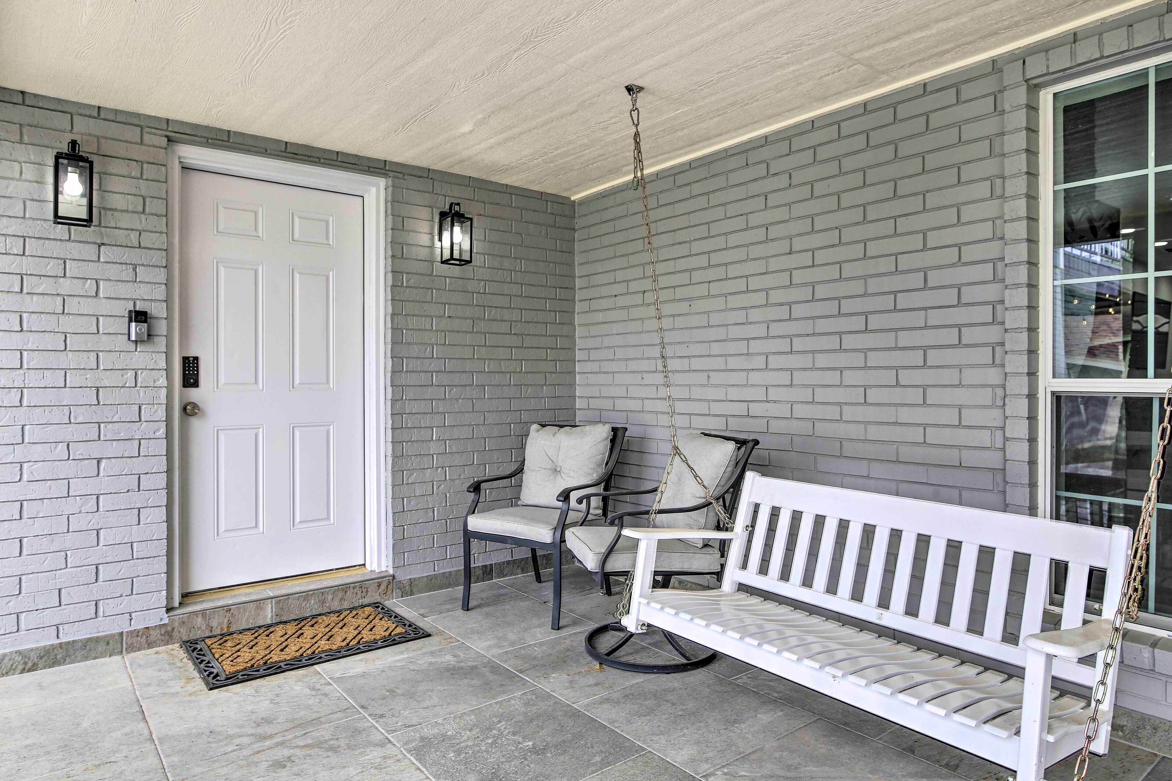 A porch with a white bench, two chairs, and a door.