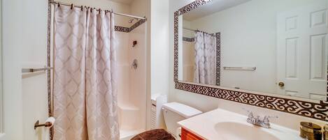 A bathroom with a shower curtain, toilet, sink, and mirror.