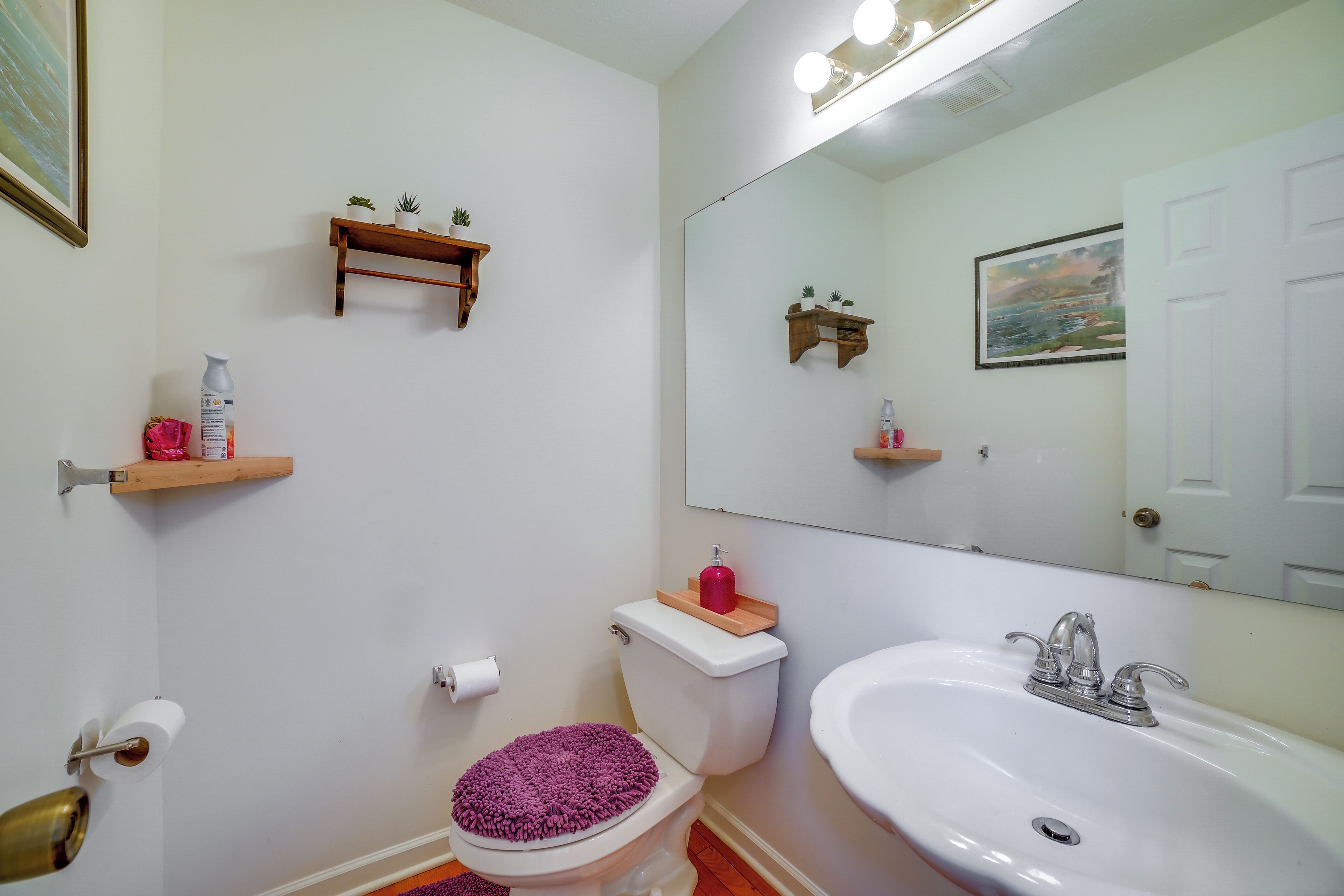 A bathroom with a toilet, sink, mirror, and shelves with toiletries.
