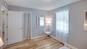 A room with a wooden floor, a white door, a white chair, a lamp, and a window with curtains. - Tracy City Home Near South Cumberland State Park! (Tracy City)
